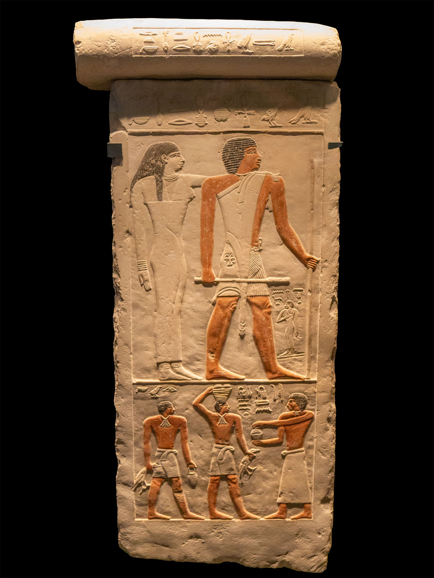 DIE EWIGE VERSORGUNG IM JENSEITS ist das beherrschende Thema dieser Scheintür. Sie zeigt den Grabherrn Anch, seine Frau Neferet-ka sowie ihre Tochter im oberen Register, darunter rechts einen Totenpriester mit Räuchergefäß und zwei Opfergabenbringer.